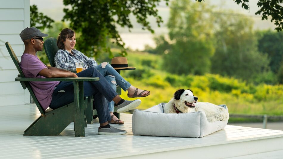 Couple assis à l’extérieur avec leur chien sur le nid douillet pour chien d’Omlet