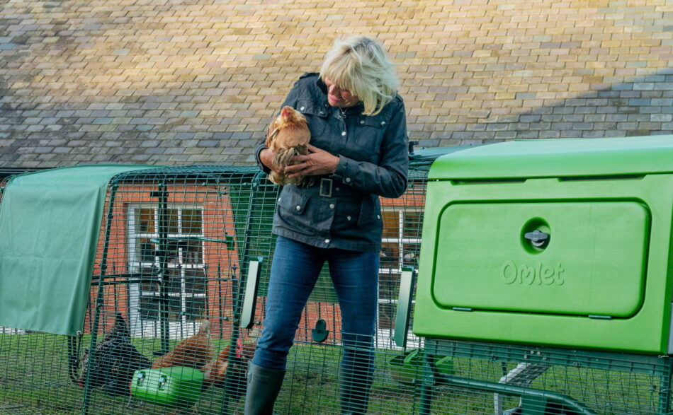 Femme qui tient une poule en sortant de l’enclos d’un poulailler Eglu Pro