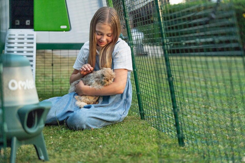 Fille qui tient une poule dans l’enclos d’un poulailler Eglu Cube Omlet