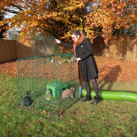 Une femme dehors en automne avec deux lapins dans leur enclos