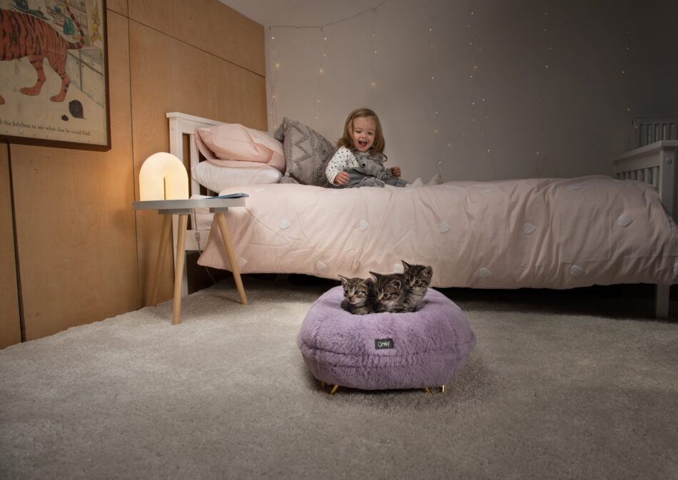 Fille assise sur un lit en train de regarder des chatons dans le panier pour chat Maya Donut couleur lilas