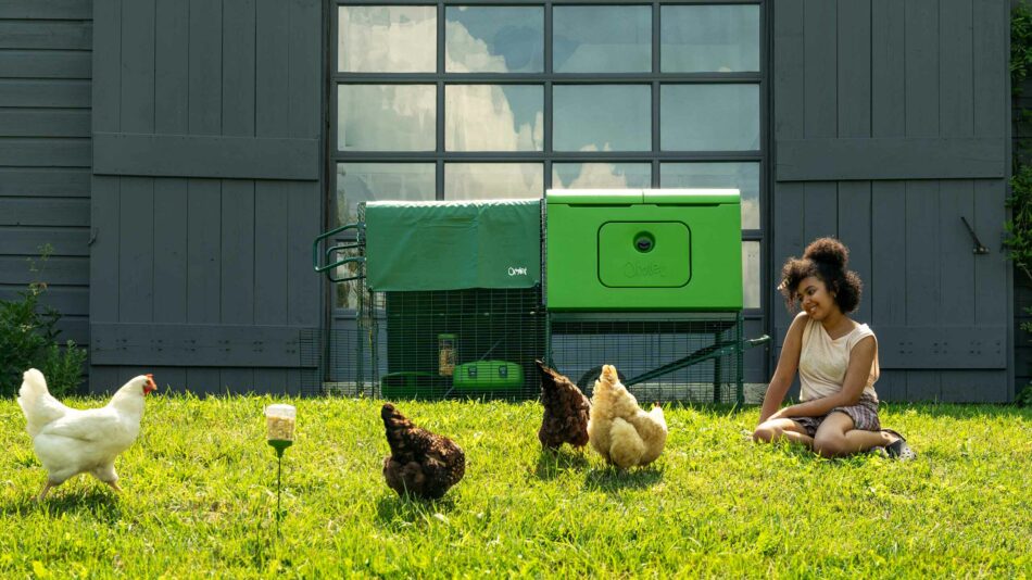 Choisissez les poules qui vous conviennent le mieux – Une fille assise avec des poules en liberté à l’extérieur du poulailler Eglu Cube