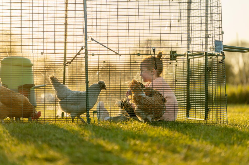 jeune fille assise avec des poules dans l’enclos d’un poulailler Eglu Pro