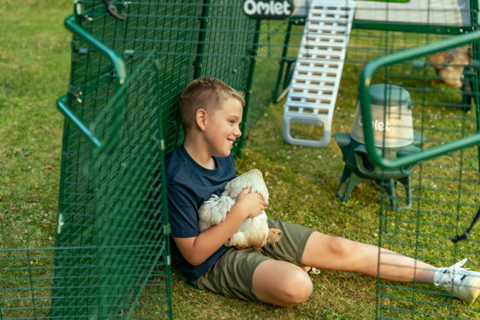 jeune garçon qui fait un câlin à une poule dans l’enclos d’un poulailler Eglu Pro