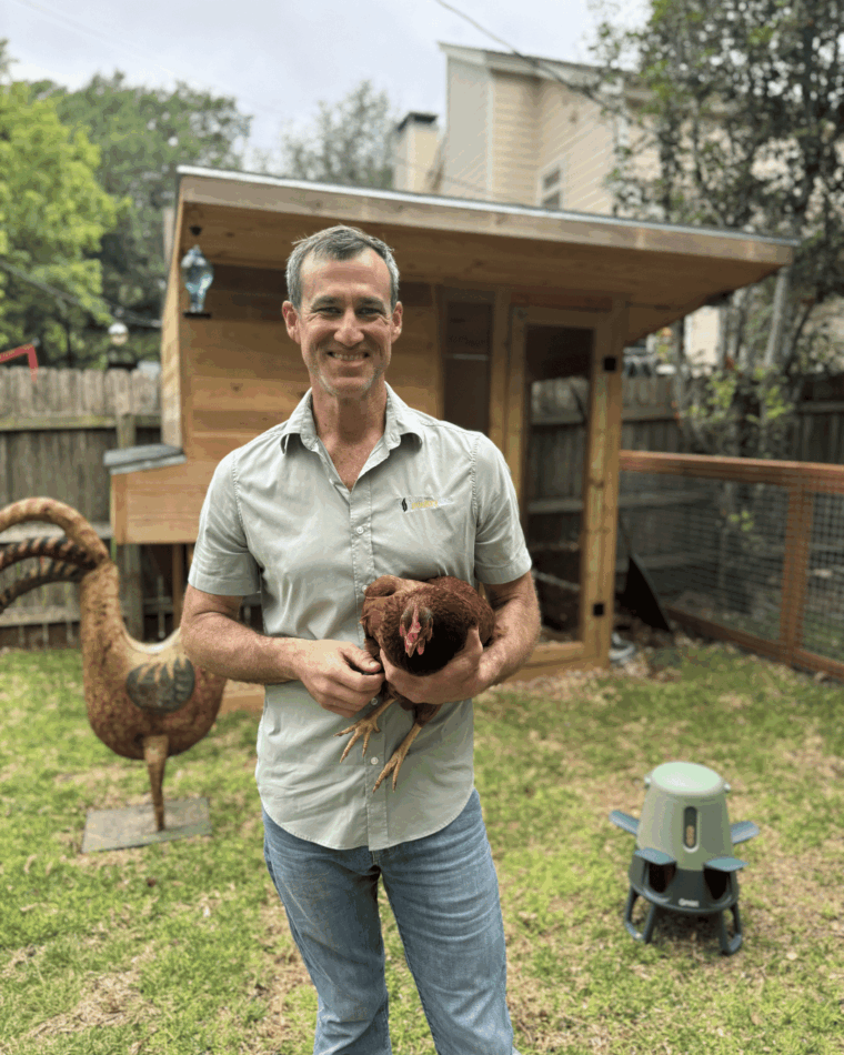 Dr Blayne dans son jardin, tenant une poule, avec l’abreuvoir intelligent d’Omlet en arrière-plan