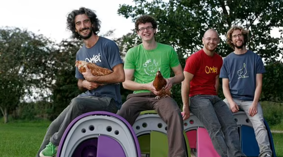 Les fondateurs d’Omlet, Hanns, James, Simon et Will, aux débuts de l’entreprise, assis sur des poulaillers avec des poules sur les genoux.